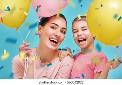 Funny Family On A Background Of Bright Blue Wall. Mother And Her Daughter Girl Are Having Fun With Balloons And Confetti. Yellow, Pink And Turquoise Colors.