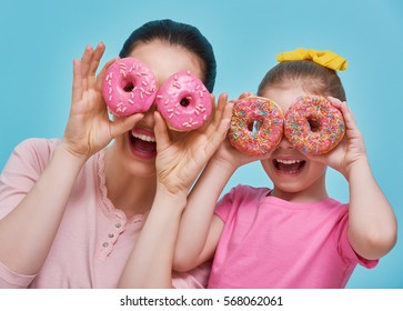 Funny Family On A Background Of Bright Blue Wall. Mother And Her Daughter Girl Are Having Fun With Colorful Donuts. Dieting Concept And Junk Food. Yellow, Pink And Turquoise Colors.