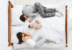 Funny Family With One Newborn Child In The Middle Of Bed, Parents Sleeping On Sides, Top View