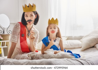 Funny family is preparing for a costume party. Mother and her child daughter girl with a paper accessories. Beautiful queen and princess in gold crowns playing together.