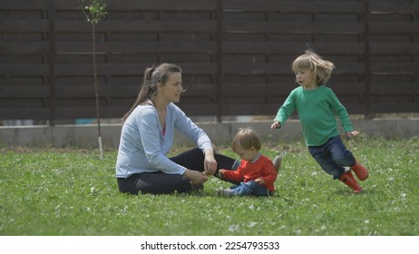 Funny family scenery, mother and baby child sit on grass, blond child run around - Shutterstock ID 2254793533