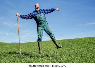 Funny farmer in his green dungarees and rubber boots is happy and makes on his sunny meadows a leap of joy.