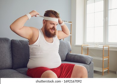 Funny fat angry man in sportswear is sitting on the sofa in the room