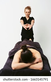 Funny fat burning massage. Portrait of cheerful woman masseur in uniforme near massage table with woman patient in wellness center. White background isolated
