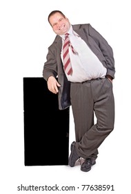 Funny Fat Businessman Standing On White Background.Friendly Fat Man In A Business Suit Stands At The Black Board. Obese Businessman With A Blank Poster On A White Background.