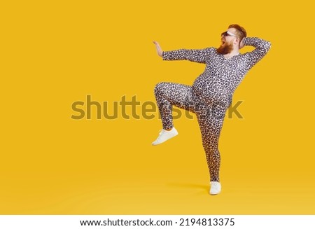 Funny fat fashion guy in pajamas posing on copy space background. Full length portrait of happy joyful plump bearded young man wearing leopard PJs dancing on blank yellow copy space background