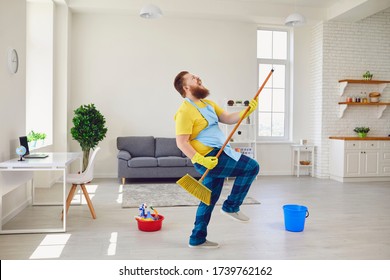 Funny Fat Man With A Beard In An Apron Dancing Cleans The Room In The House.