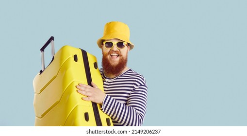 Funny fat man going on vacation. Cheerful traveler leaving for summer holiday. Portrait of happy excited bearded guy in striped swimsuit, bucket hat, and sunglasses holding yellow suitcase and smiling