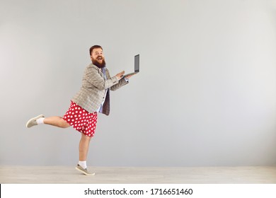 Funny Fat Man In A Jacket Works Using A Laptop While Dancing On A Gray Background.