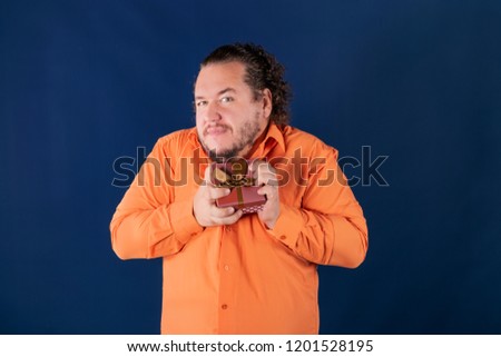 Funny fat man in orange shirt opens a box with a gift