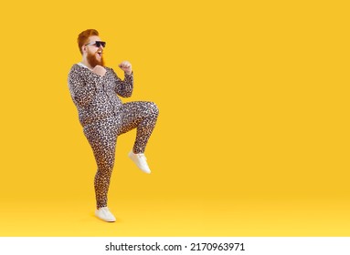 Funny Fat Redhead Man In Animal Print Pajama Dancing On Yellow Studio Background. Smiling Overweight Red-haired Guy In Cool Suit Perform Winner Dance Celebrate Success. Copy Space.