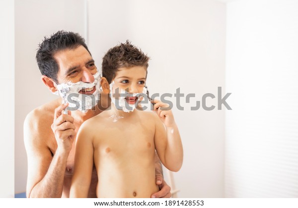 Funny father and son shaving in the bathroom. Focus\
on kid.