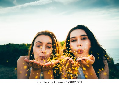 Funny female friends blowing golden glitter over a cliff at dusk - Powered by Shutterstock