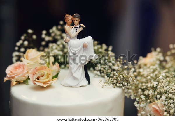 Funny figurines suite at a luxury wedding white\
cake decorated with fresh\
flowers.