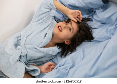 Funny Five Year Old Boy With Long Hair Is Lying In A Blue Terry Dressing Gown On The Bed