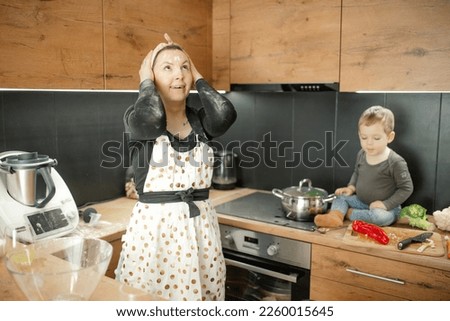 Funny floury shocked woman in handkerchief look up, holding head near little boy in flour because of mess in the kitchen