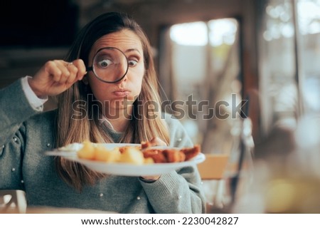 
Funny Food Critic Checking the Restaurant Dish with a Magnifying Glass. Picky eater analyzing the ingredients in a meal course
