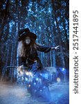 Funny forest witch sorceress with red hair, dressed in a black dress and a big hat, stands with her broom in the forest. Magic tales. Halloween. Fantasy.