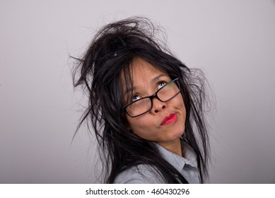 Funny, frazzled looking Asian woman with bright lipstick and ruffled hair pulling a face while looking up.
