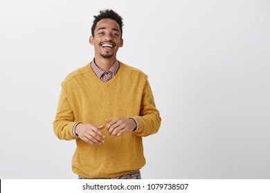 Funny friend tells hilarious jokes. Indoor shot of pleased happy african-american in stylish outfit smiling broadly and gesturing over chest during conversation, having nice talk with coworker