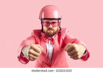 Funny furious tough driver holding pretend steering wheel. Studio shot of man with ginger beard and angry face, wearing pink helmet, funky modern suit, bow tie and sunglasses driving his invisible car - Shutterstock ID 2132211523