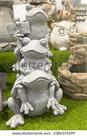 Funny garden sculptures. Decorations for the garden or decoration of the exterior of the house. 3 concrete frogs on top of each other with a welcome sign. Garden care concept.