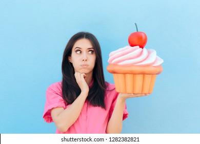 Funny Girl with Big Cupcake Thinking of her Diet. Woman holding big backed dessert on cheat day  