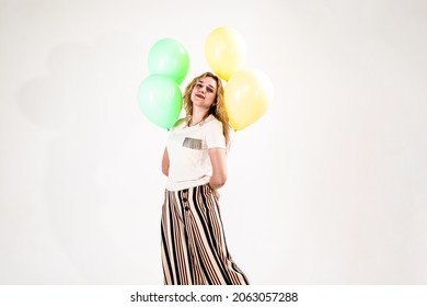 Funny girl, blonde, in a light T-shirt and striped trousers-skirt. a girl stands barefoot with balloons in her hands on a white background.