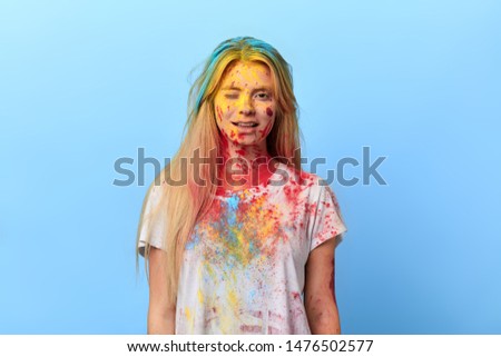 funny girl with colorful face giving a wink. close up portrait, fun, flirt concept. isolated blue background, studio shot