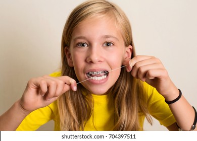 Funny Girl With Dental Braces Flossing Her Teeth. Close-up Portrait Of Pre Teen Girl With Dental Floss Isolated.