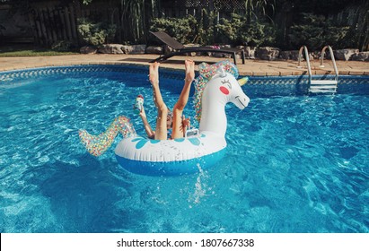 Funny Girl Dropped Fell From Inflatable Ring Unicorn. Kid Child Enjoying Having Fun In Swimming Pool. Summer Outdoor Water Activity For Kids. Legs Up In The Air In Pool Water.