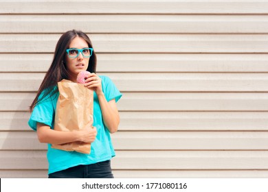 Funny Girl Eating Donuts Strait Out Of A Paper Bag. Compulsive Eater Feeling Guilty While Snacking On Sweets
