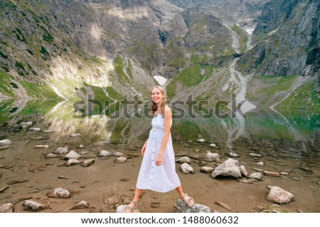 Funny girl with facial expression posing in white dress in lake with reflections under Mount Rysy in Polish Tatra
