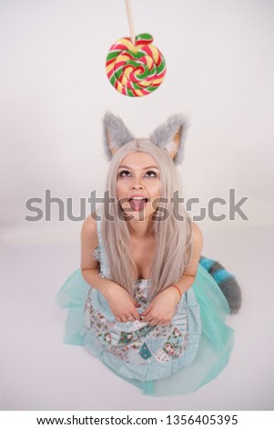 funny girl with fluffy fur cat ears stands in a kitchen apron on knees and serves as a slavery kitty to get candy on a white background in the Studio