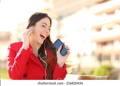 Funny Girl Listening To The Music With Earphones From A Smart Phone With An Urban Unfocused Background