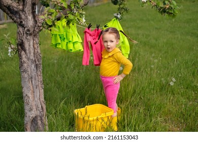A funny girl with pigtails helps her mother hang wet clothes after laundry on a clothesline in the fresh air in the garden. Drying after washing
