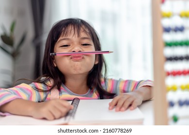 funny girl playing holding pen between nose and lips as mustache looking at the camera, playful bored after learning long hours.