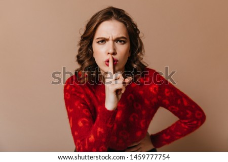 Funny girl in red sweater touching lips with finger. Studio shot of woman requiring silence.
