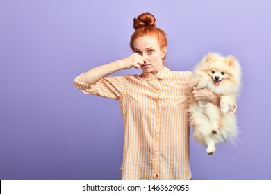funny girl with stylish striped shirt closing her nose, as the dog is farting. close up portrait. unpredictable situation, isolated blue background, studio shot.