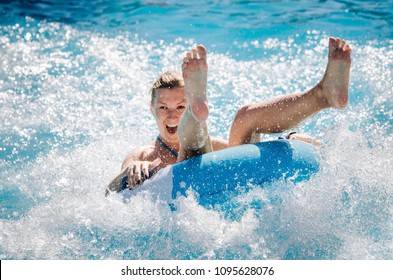 Garota engraçada tomando um passeio de água rápido em um flutuador espirrando água. Férias de verão com conceito de parque aquático.