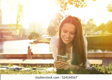 Funny Girl Using A Smart Phone On The Grass Of A Park With A Green Background