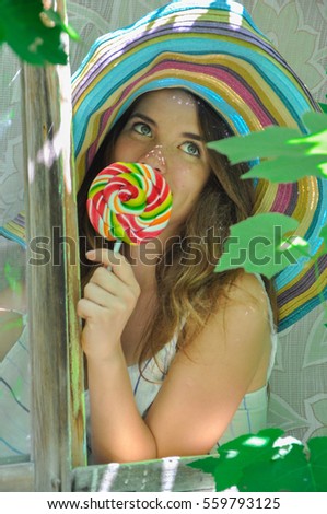 funny girl wearing a colorful hat with lollipop in a window with grape leaves in high quality