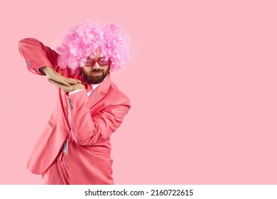 Funny Goofy Bearded Adult Man Wearing Pink Party Suit, Curly Clown Wig And Funky Sunglasses Dancing Isolated On Blank Empty Solid Pink Background With Copy Space On Right Side