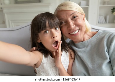 Funny granddaughter holding camera taking self-portrait photo with elderly 60s grandmother close up view faces webcam view, older younger generation record video having fun using modern gadget concept