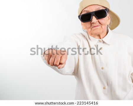 Funny grandma's studio portrait  wearing eyeglasses and baseball cap who kicks with  her fist , isolated on white