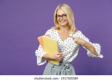 Funny Gray-haired Blonde Teacher Woman Lady 40s 50s Years Old In White Dotted Blouse Eyeglasses Standing Pointing Index Finger On Notepads Isolated On Bright Violet Color Background Studio Portrait