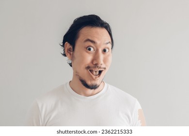 Funny grinning smile face of Asian man in white t-shirt and grey background.