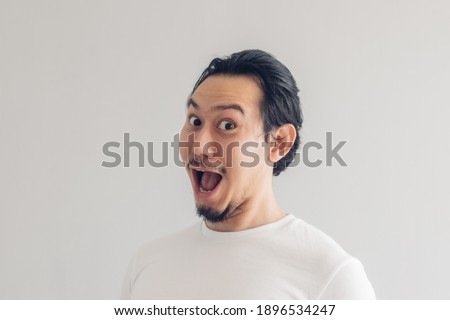 Funny grinning smile face of Asian man in white t-shirt and grey background.