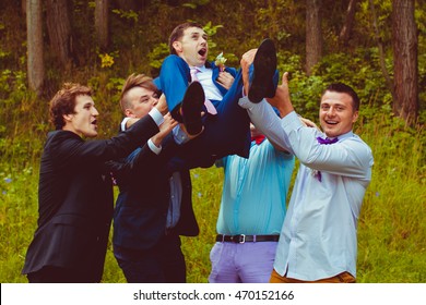 Funny Groomsmen In Colored Bows Hold Scared Groom In The Air