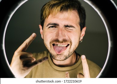 Funny Guy Posing Behind A Ring Light. Studio Photography. Male Model Having Fun At Studio. Rock And Roll Sign. Happy Man Celebrating His Success. Handsome Guy Looking Camera And Having Fun.